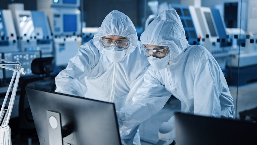 Eyelit Research Factory Cleanroom: Engineer and Scientist Wearing Coveralls Talk and Work on Computer, Use Microscope to Inspect Motherboard Microprocessor, Develop Electronics for Medical Electronics